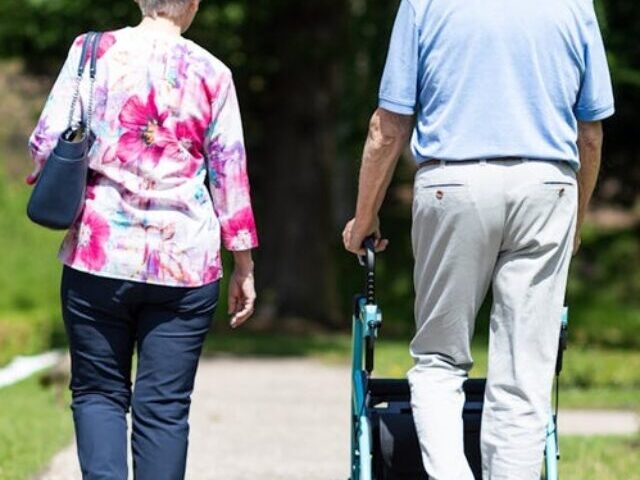 Representative Image: Two People Walking in a Park. Elderly couple walking along a pathway in a park or garden. The man is using a walker for support, while the woman walks beside him. Photo Source: Rollz International (Pexels)