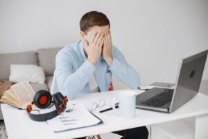 Person seated at a desk with laptop and work items, representing employment transition pressure.