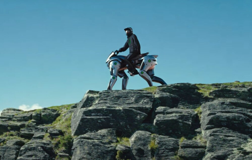 A person riding what appears to be a futuristic robotic horse or a mechanical quadruped on a rocky hilltop under a clear blue sky. Photo Source: Kawasaki Group Channel (YouTube)