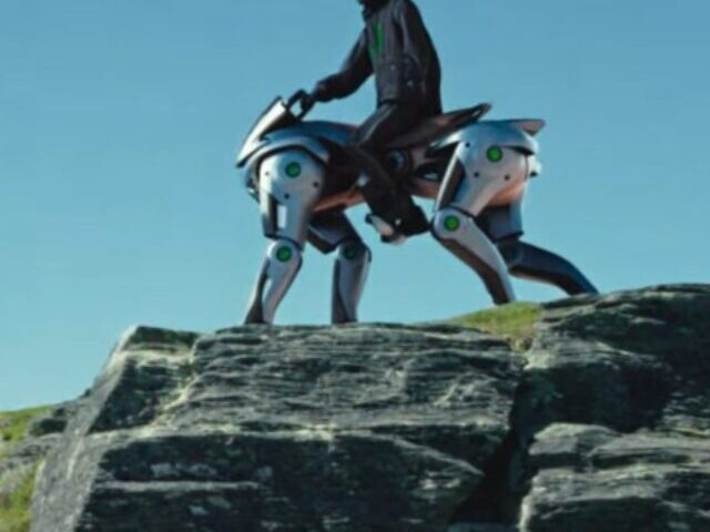 A person riding what appears to be a futuristic robotic horse or a mechanical quadruped on a rocky hilltop under a clear blue sky. Photo Source: Kawasaki Group Channel (YouTube)