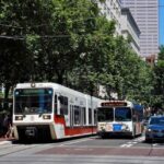 An inbound MAX train being passed by a bus. Image Source: Steve Morgan (CC BY-SA 3.0)