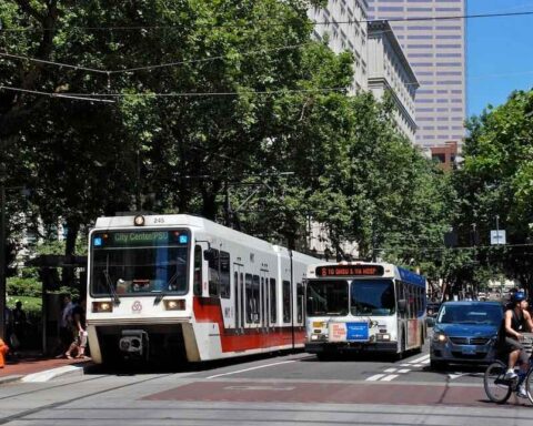 An inbound MAX train being passed by a bus. Image Source: Steve Morgan (CC BY-SA 3.0)