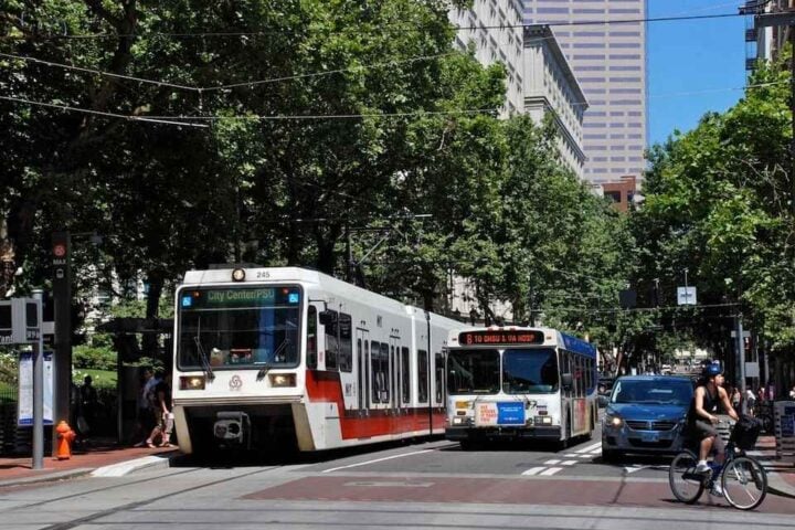 An inbound MAX train being passed by a bus. Image Source: Steve Morgan (CC BY-SA 3.0)