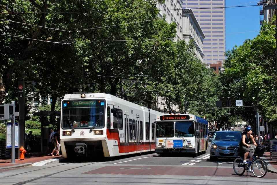 An inbound MAX train being passed by a bus. Image Source: Steve Morgan (CC BY-SA 3.0)