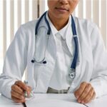 Doctor writing patient notes while sitting at a desk in a medical office.