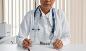 Doctor writing patient notes while sitting at a desk in a medical office.