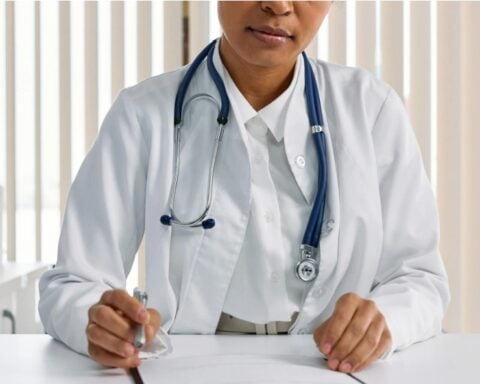 Doctor writing patient notes while sitting at a desk in a medical office.