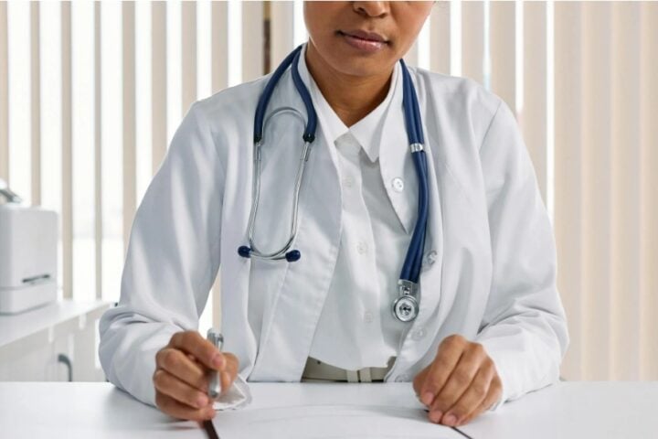 Doctor writing patient notes while sitting at a desk in a medical office.