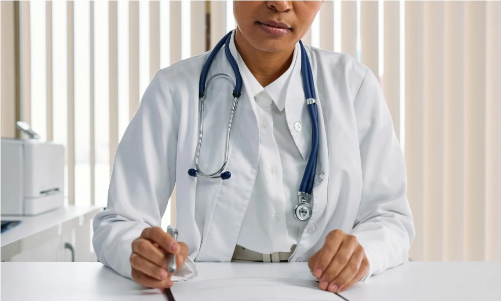 Doctor writing patient notes while sitting at a desk in a medical office.