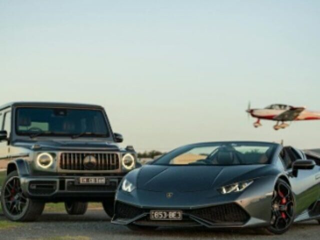 Two luxury black cars parked on an empty asphalt road under a clear sky