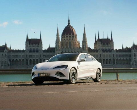 A white BYD Seal electric sedan parked beside the Danube River in front of the Hungarian Parliament Building in Budapest.