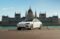 A white BYD Seal electric sedan parked beside the Danube River in front of the Hungarian Parliament Building in Budapest.