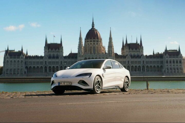 A white BYD Seal electric sedan parked beside the Danube River in front of the Hungarian Parliament Building in Budapest.
