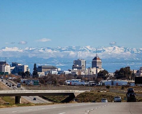 Alt Text: Downtown Fresno skyline with snow-capped Sierra Nevada mountains under a clear blue sky.