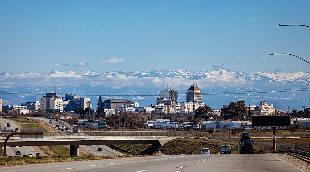 Alt Text: Downtown Fresno skyline with snow-capped Sierra Nevada mountains under a clear blue sky.