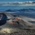 Panoramic view of barren volcanic cones, craters, and lava fields on Russia’s Kamchatka Peninsula beneath a cloudy sky, illustrating the region’s active tectonic setting.