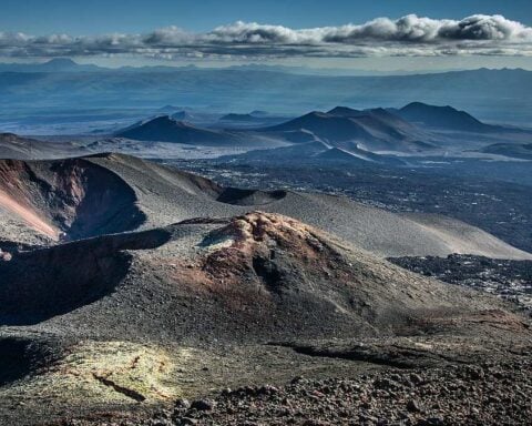 Panoramic view of barren volcanic cones, craters, and lava fields on Russia’s Kamchatka Peninsula beneath a cloudy sky, illustrating the region’s active tectonic setting.