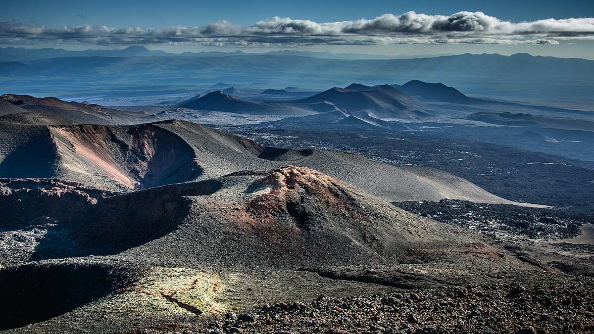 Panoramic view of barren volcanic cones, craters, and lava fields on Russia’s Kamchatka Peninsula beneath a cloudy sky, illustrating the region’s active tectonic setting.