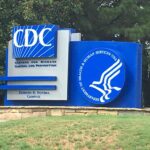 Photograph of the blue-and-white “Centers for Disease Control and Prevention” sign at the Edward R. Roybal Campus, with the Department of Health and Human Services logo and a background of trees.