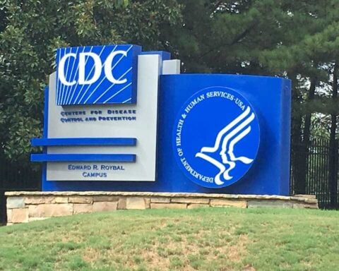 Photograph of the blue-and-white “Centers for Disease Control and Prevention” sign at the Edward R. Roybal Campus, with the Department of Health and Human Services logo and a background of trees.