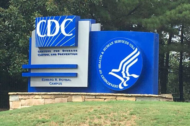 Photograph of the blue-and-white “Centers for Disease Control and Prevention” sign at the Edward R. Roybal Campus, with the Department of Health and Human Services logo and a background of trees.