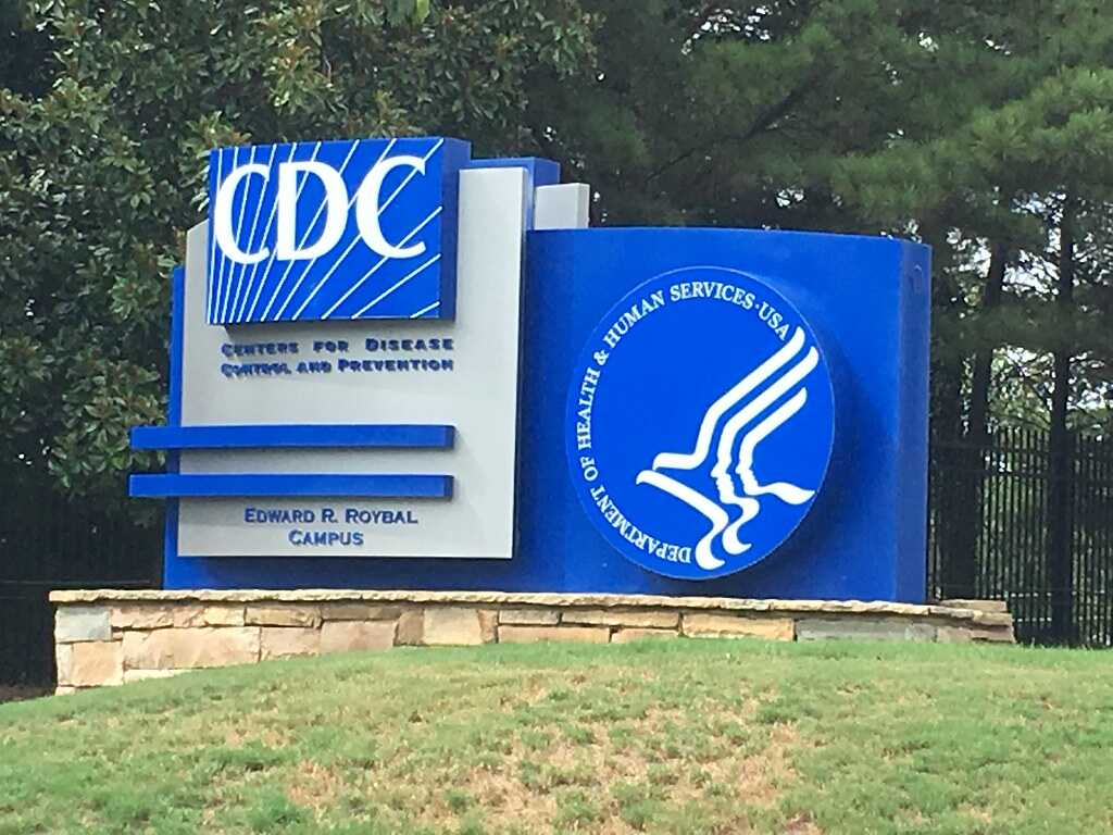 Photograph of the blue-and-white “Centers for Disease Control and Prevention” sign at the Edward R. Roybal Campus, with the Department of Health and Human Services logo and a background of trees.