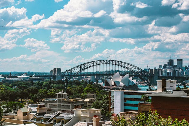 View over Potts Point rooftops to the Sydney Harbour Bridge and Opera House under a partly cloudy sky.