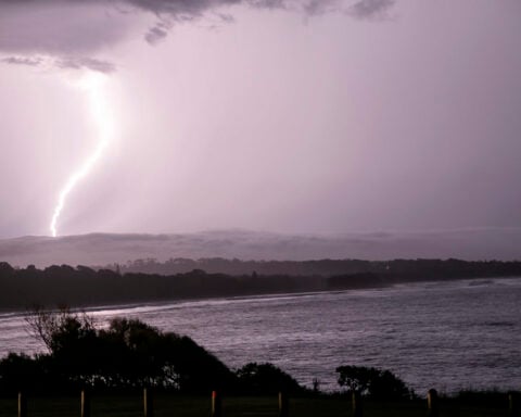 A bright lightning bolt strikes the ocean off a darkened NSW shoreline under a stormy sky.