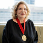 Portrait of Wallis Annenberg wearing her National Humanities Medal, smiling against a blurred urban backdrop.