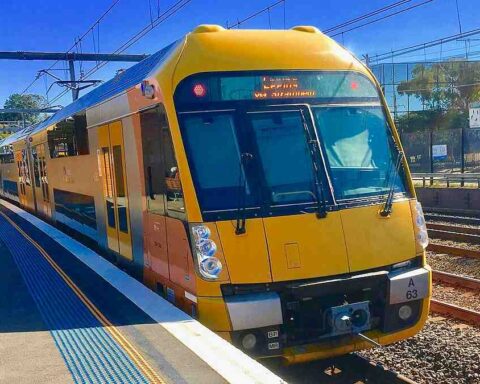 A yellow-and-steel Sydney Trains Waratah A-set (A63) standing at a suburban platform under overhead wires and clear blue sky. Photo Source: Trainsandtech (CC BY-SA 4.0)