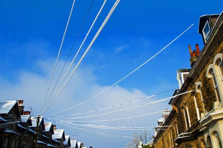 Snow-covered power lines above a row of brick houses, illustrating the network infrastructure underpinning every home’s energy bill.
