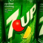 Two green 7Up soda cans showing the tropical flavor variant branding with crisp clean refreshing text and 100% natural flavors labeling
