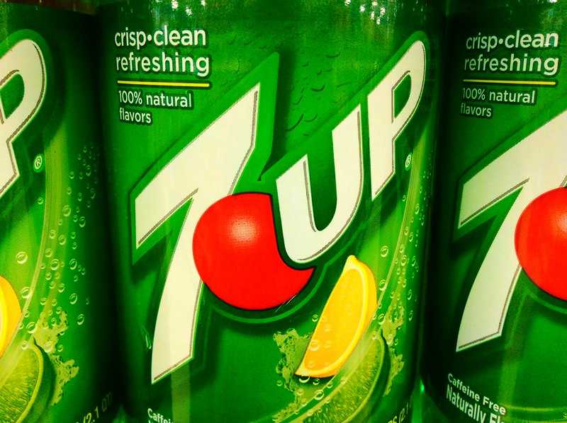 Two green 7Up soda cans showing the tropical flavor variant branding with crisp clean refreshing text and 100% natural flavors labeling