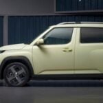 Side profile of a light-green Hyundai Inster EV parked indoors against a corrugated metal-panel backdrop.