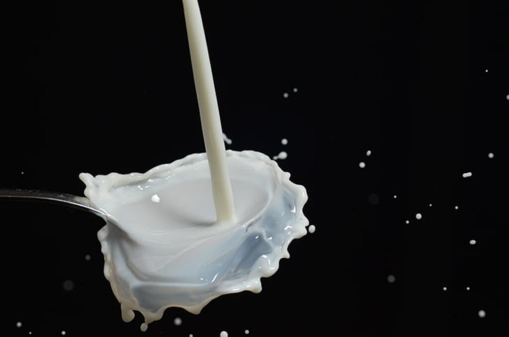 Close-up shot of white milk pouring into a silver spoon, with splashing droplets frozen in mid-air against a black background.