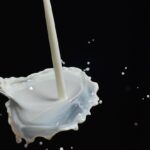 Close-up shot of white milk pouring into a silver spoon, with splashing droplets frozen in mid-air against a black background.