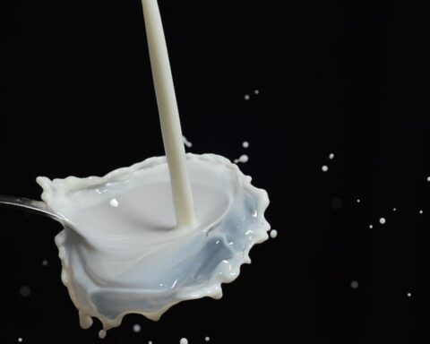 Close-up shot of white milk pouring into a silver spoon, with splashing droplets frozen in mid-air against a black background.
