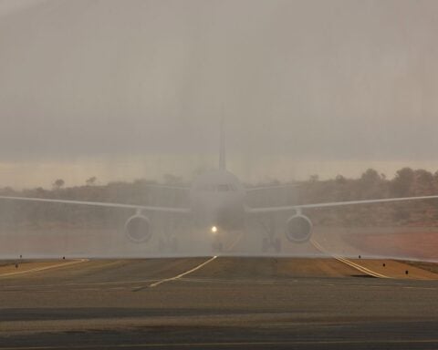 Water cannon salute creating an arch of water over an airport runway with aircraft visible in the distance at sunset