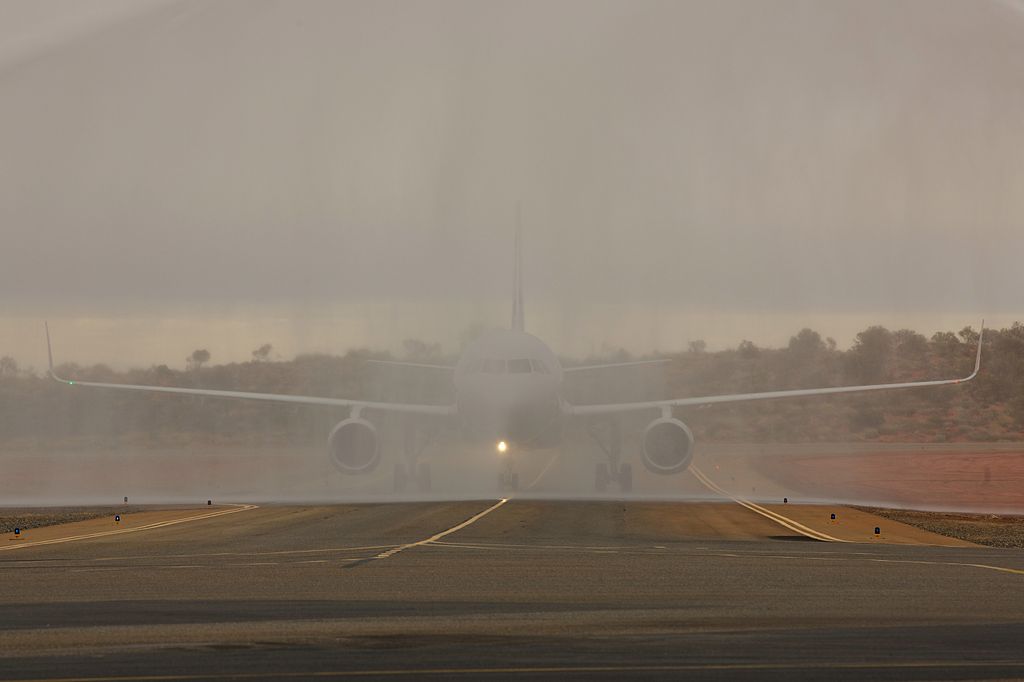 Water cannon salute creating an arch of water over an airport runway with aircraft visible in the distance at sunset