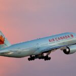 Air Canada Boeing 777-200LR aircraft taking off from Toronto Pearson Airport with sunset sky background.