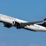 Air Canada Boeing 737 MAX‑8 aircraft in mid‑flight with clear sky in background, featuring white fuselage, black tail, and red maple leaf logo.