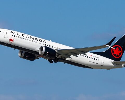 Air Canada Boeing 737 MAX‑8 aircraft in mid‑flight with clear sky in background, featuring white fuselage, black tail, and red maple leaf logo.