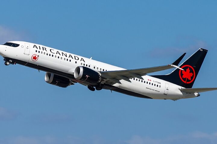 Air Canada Boeing 737 MAX‑8 aircraft in mid‑flight with clear sky in background, featuring white fuselage, black tail, and red maple leaf logo.