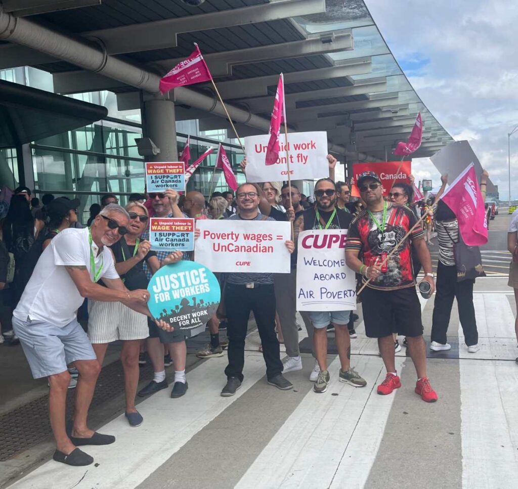 Air Canada flight attendants and supporters protest wage theft and unpaid pre-boarding duties outside an airport terminal, holding CUPE and Justice for Workers signs.