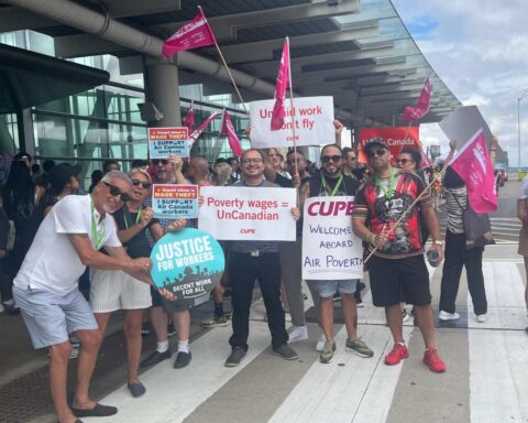 Air Canada flight attendants and supporters protest wage theft and unpaid pre-boarding duties outside an airport terminal, holding CUPE and Justice for Workers signs.