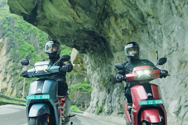 Two Ampere Nexus electric scooters riding along a mountainous road near Shipki La Pass, with rugged rocky terrain and riders in protective gear, showcasing the scooters’ endurance and design.