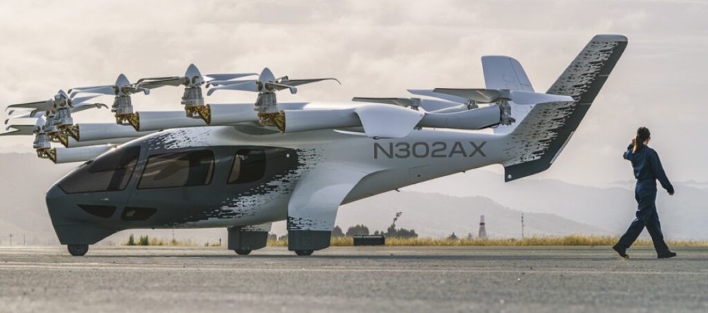 Archer Aviation's white Midnight eVTOL aircraft, registration N703AX, in mid-flight against a clear blue sky.