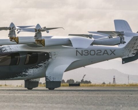Archer Aviation's white Midnight eVTOL aircraft, registration N703AX, in mid-flight against a clear blue sky.