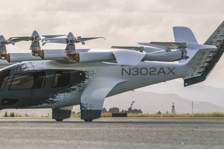Archer Aviation's white Midnight eVTOL aircraft, registration N703AX, in mid-flight against a clear blue sky.