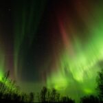 Illustrative aurora borealis (northern lights) glowing over a dark northern horizon under clear skies.